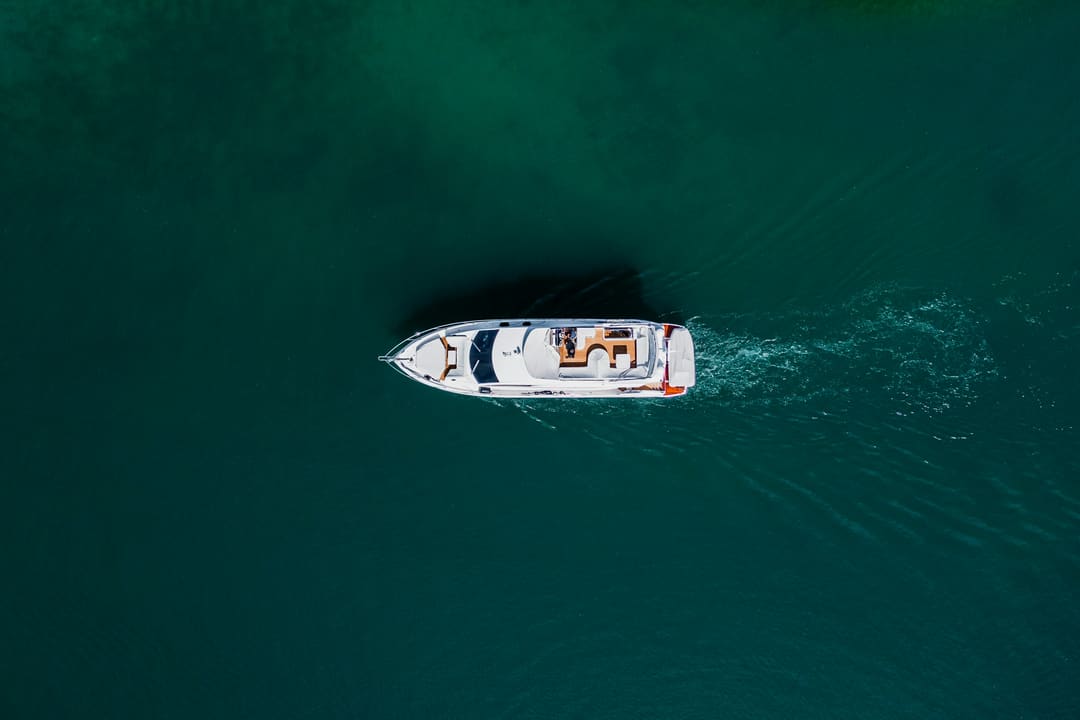 Yate a motor visto desde arriba, cruzando agua verde azulada oscura.