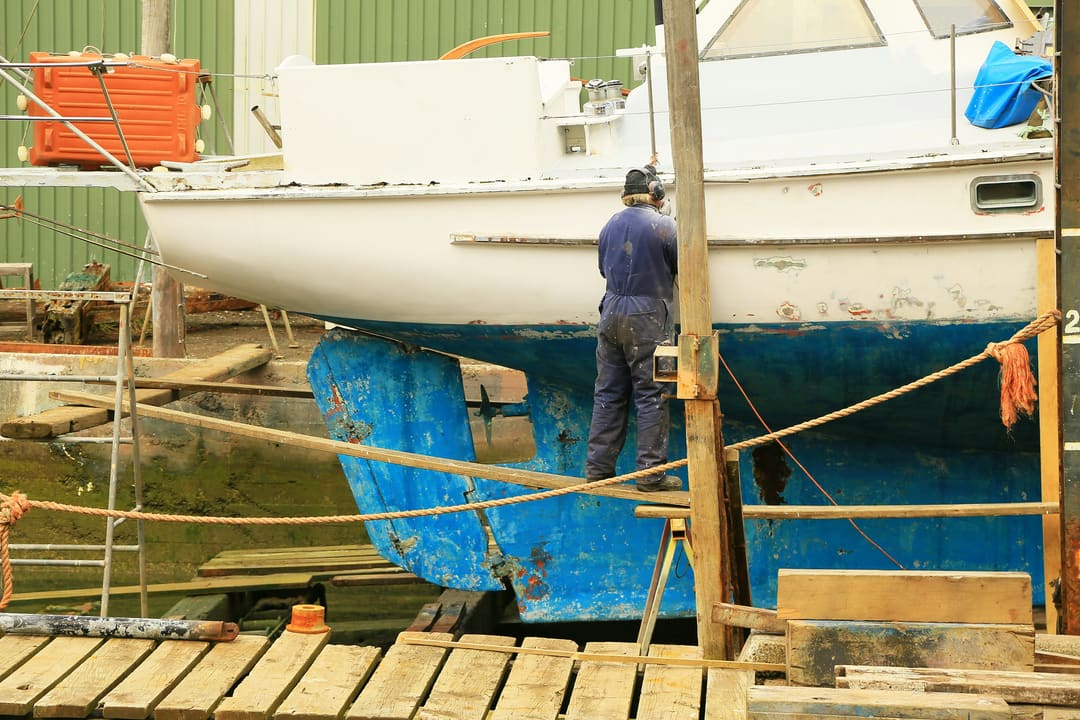 Operario de espaldas trabajando en el casco de un velero en varadero.